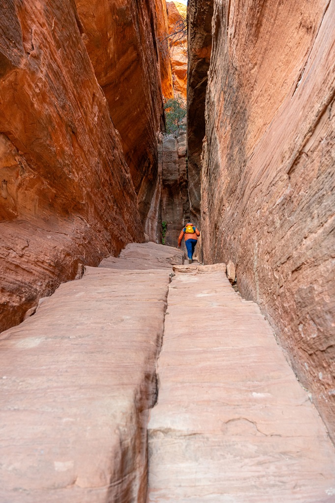 Woman climbing up the middle rocky chute to get inside the Subway Cave in Sedona.