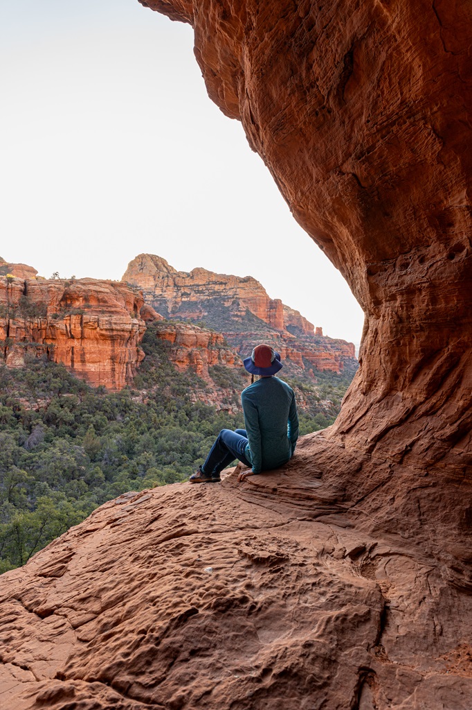 Woman sitting near a ledge inside the Subway Cave looking at the views of beautiful red rock formations in the distance.