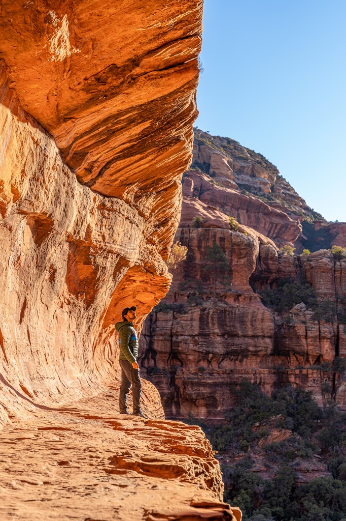 Man standing on the left side inside the Subway Cave with the sun shining making the cave glow a bright orange.