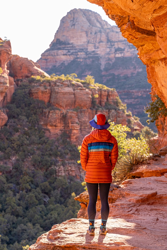 Woman standing on a wide rocky ledge near the cliff dwellings at the Subway Cave in Sedona.