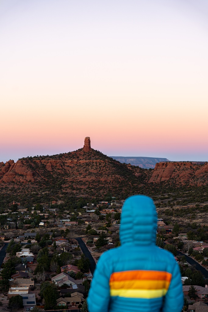 Woman standing on Sugarloaf Mountain in Sedona watching the sunrise with Chimney Rock in the distance.