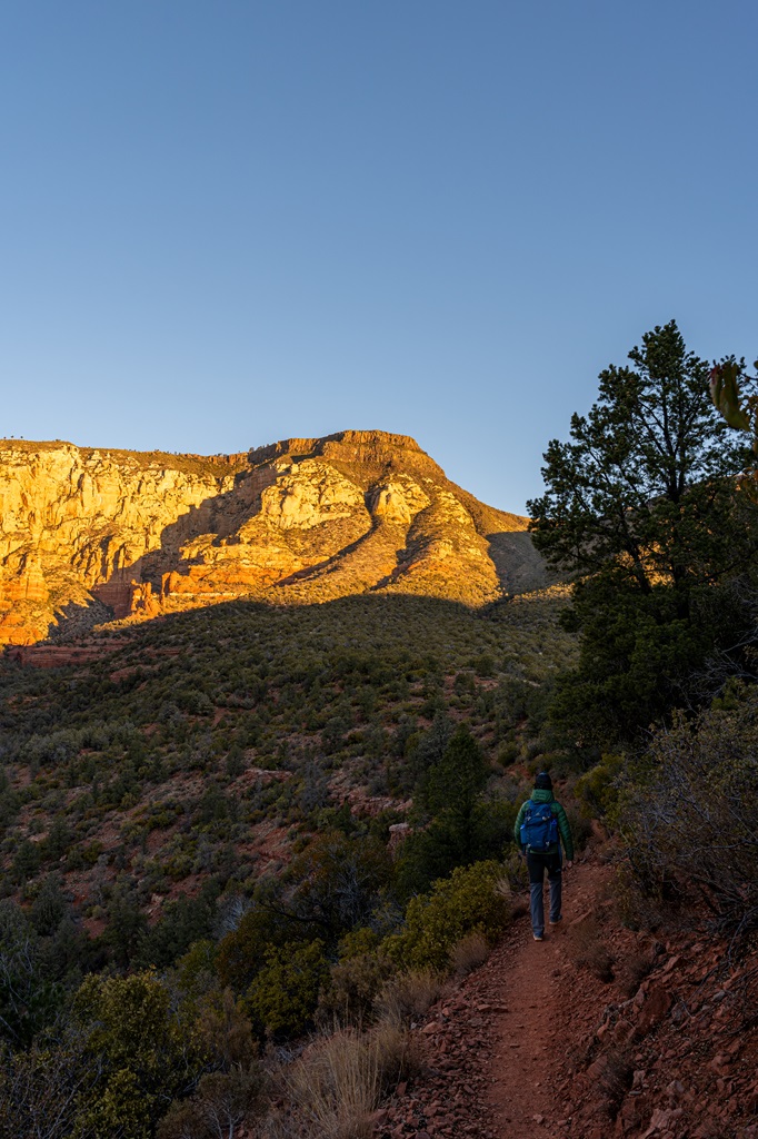 Man hiking along the Wilson Mountain Trail with Wilson Mountain in the distance being illuminated by the sun.