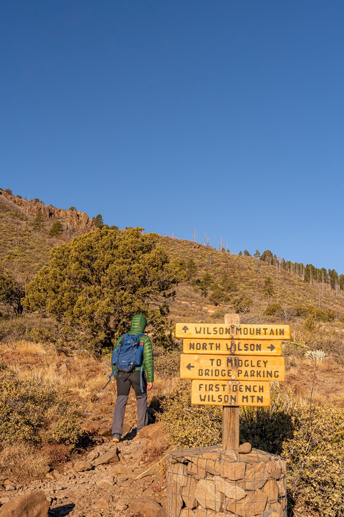 Man hiking past the First Bench of Wilson Mountain trail sign in Sedona towards the summit.