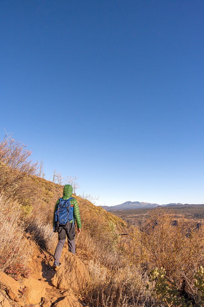 Man hiking towards the top of Wilson Mountain with San Francisco Peaks in the distance.