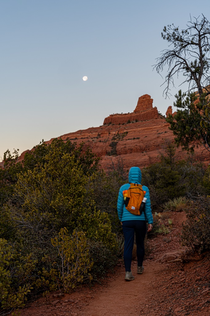 Woman hiking along the Wilson Mountain Trail before sunrise with a full moon in the sky.