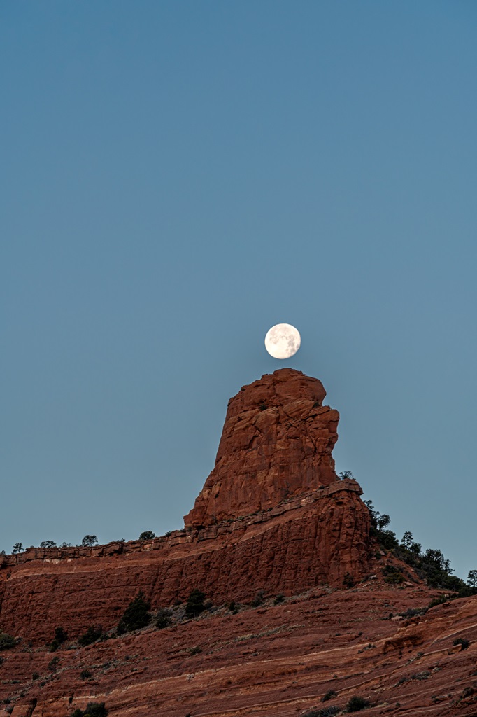 Full moon positioned directly over a unique pointy rocky formation seen from the Wilson Mountain Trail in Sedona.