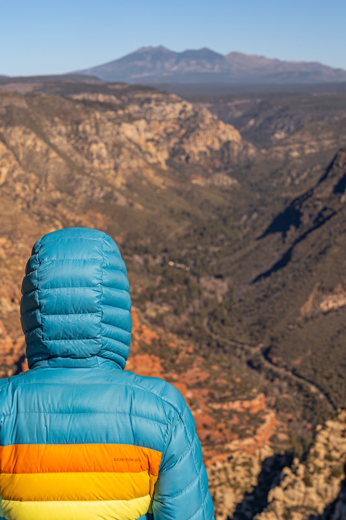 Woman standing at the North Canyon Overlook in Sedona looking out at the views with San Francisco Peaks in the distance.