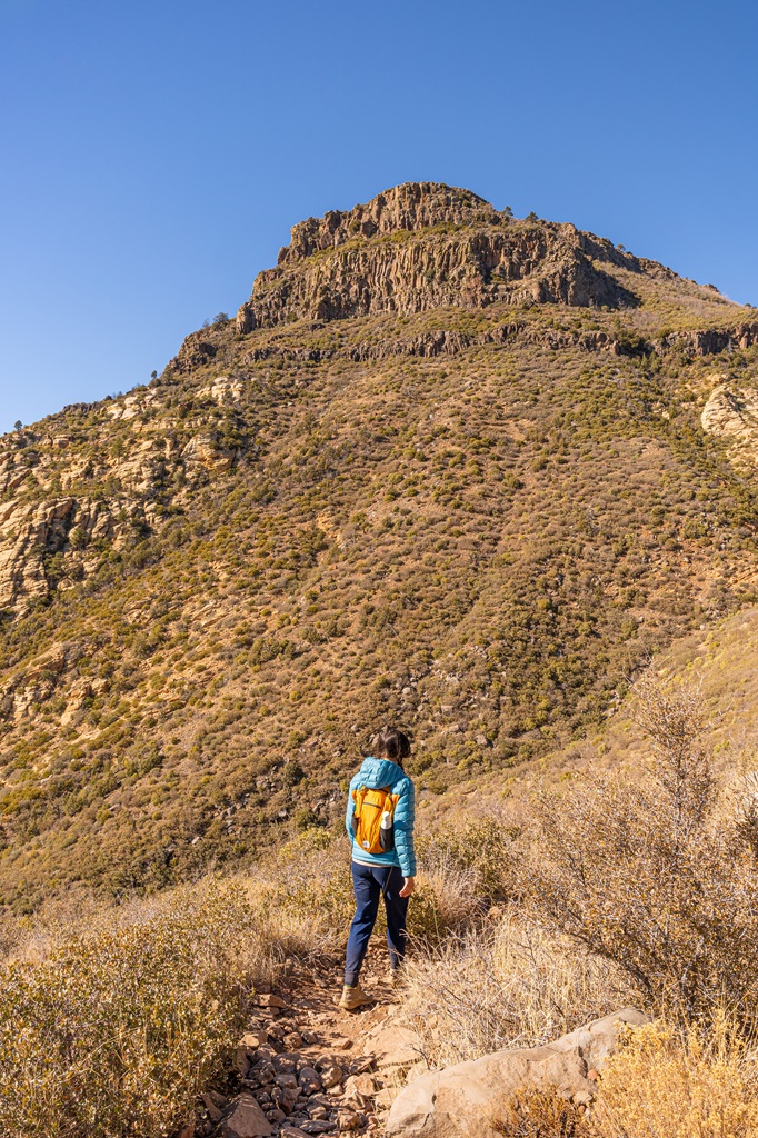 Woman hiking down the Wilson Mountain Trail in Sedona with Wilson Mountain in the background.