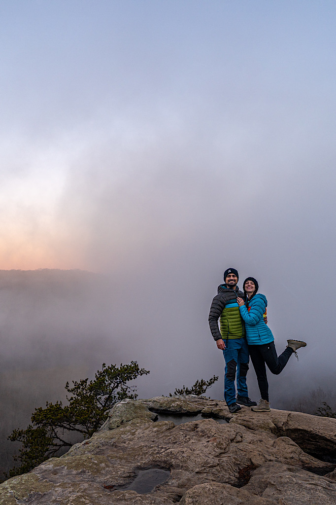 Man and woman posing for a picture on Long Point Overlook during sunrise with dense fog rolling in.