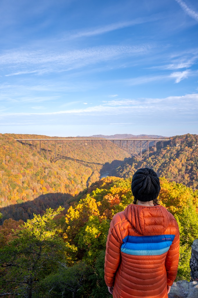 Woman standing at the Long Point Overlook looking at the fall colors covering the landscape and New River Gorge Bridge in the middle.