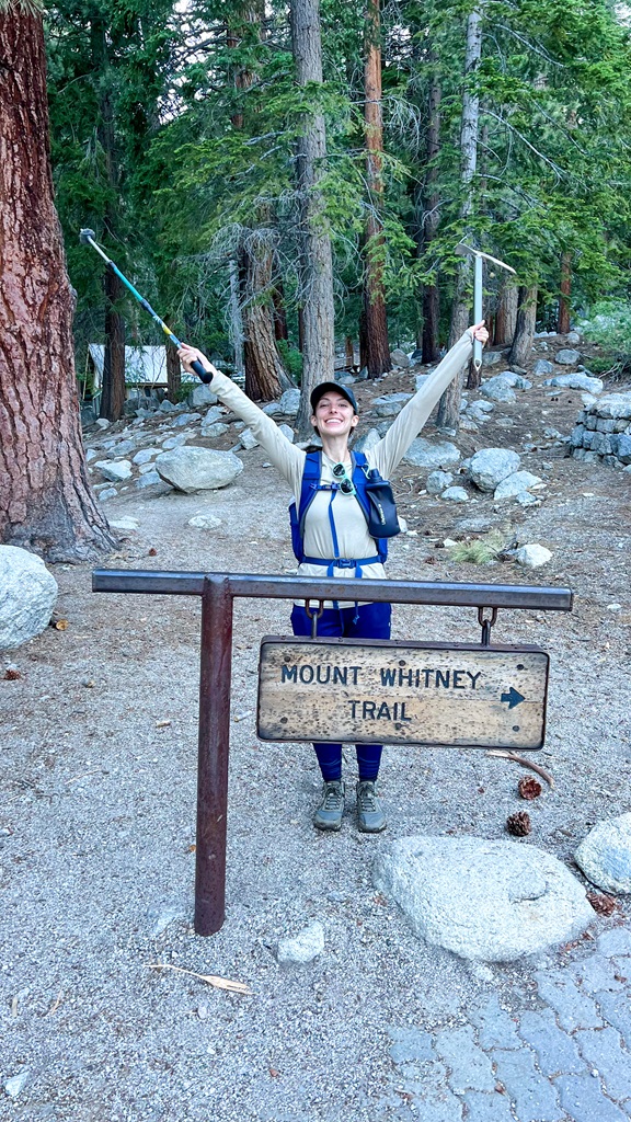 Woman posing behind the Mount Whitney Trailhead sign after hiking Mt Whitney in a day.