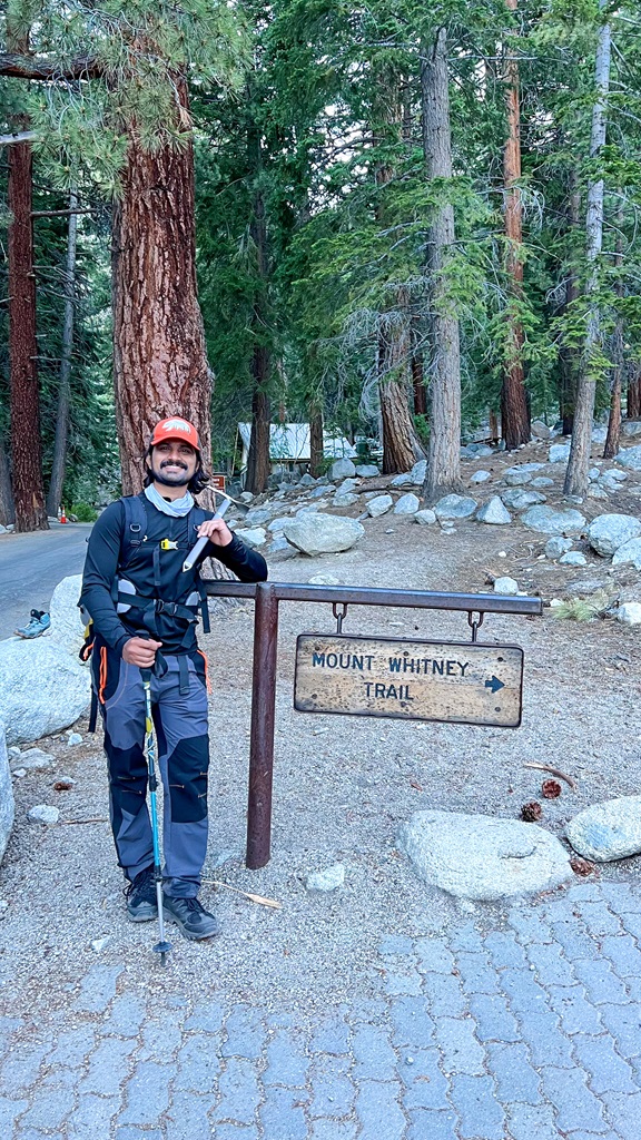 Man posing beside the Mount Whitney Trailhead sign after hiking Mt Whitney in a day.