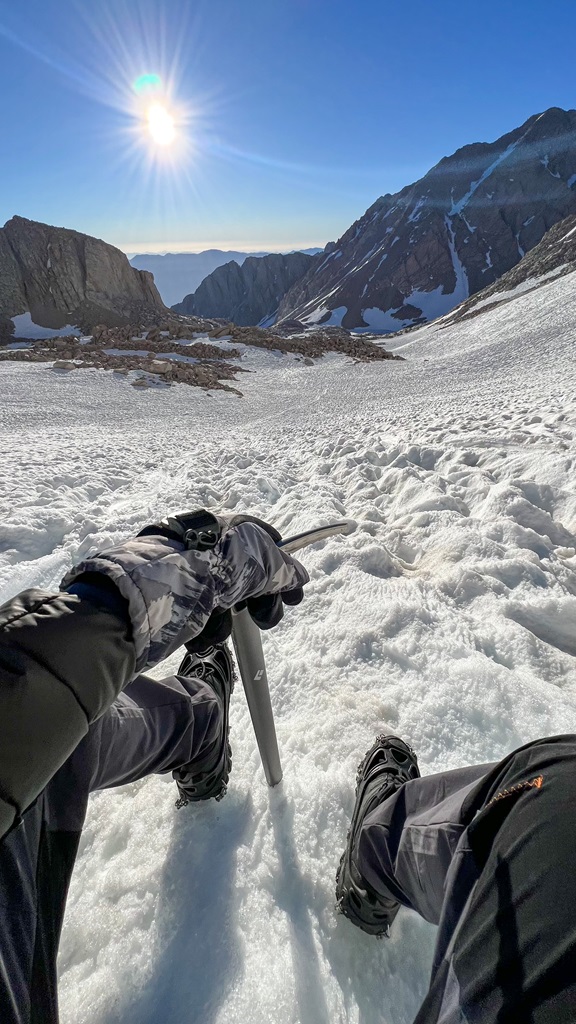 Man resting on the steep, snowy chute near the summit of Mt Whitney.