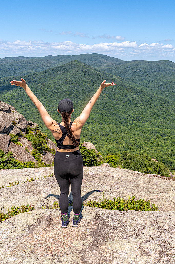 Woman standing on the summit of Old Rag Mountain with hands in the air in August.