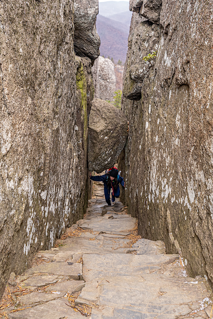 Woman climbing up a naturally formed staircase with a bolder wedged between the rock walls along the Old Rag Rock Scramble.