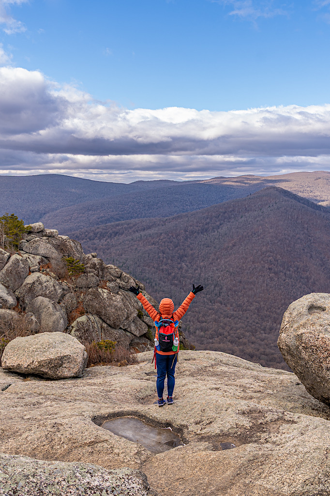 Woman standing on the summit of Old Rag Mountain with hands in the air in January.