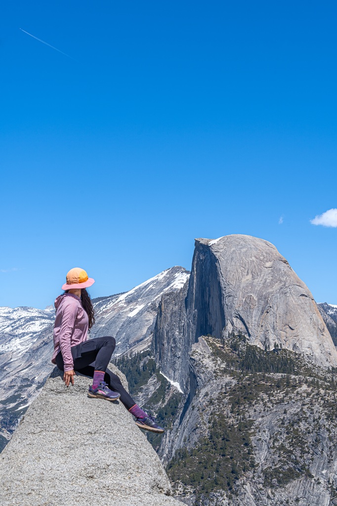 Woman sitting on a rock looking at Half Dome from Glacier Point in Yosemite National Park.