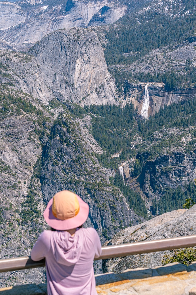 Woman looking at the views of Liberty Cap, Nevada Fall, and Vernal Fall from Glacier Point Overlook in Yosemite National Park.