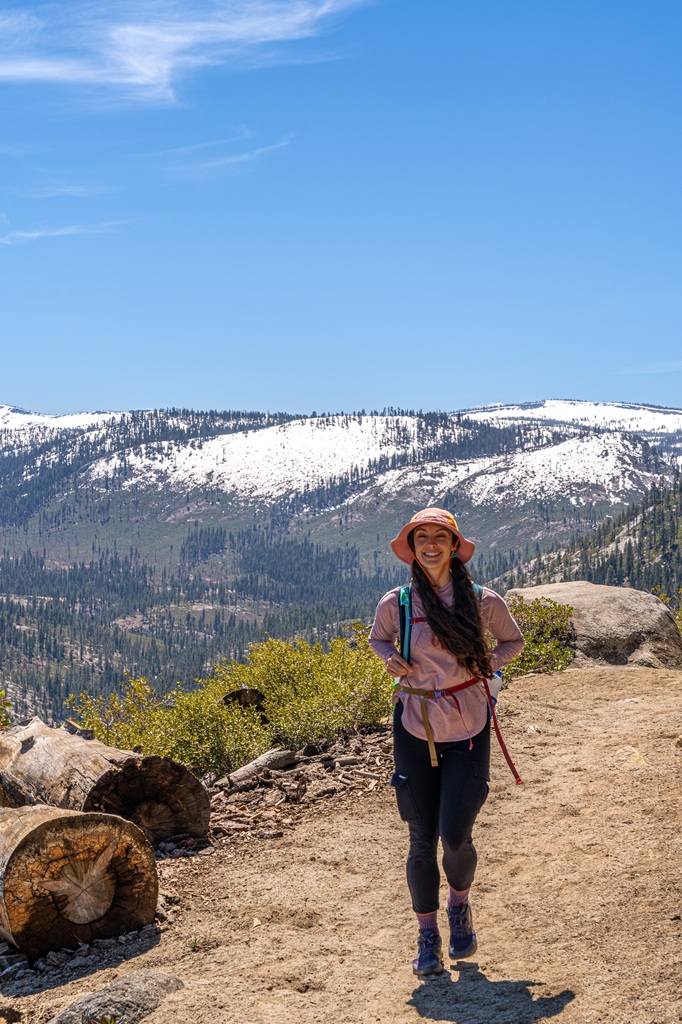 Woman hiking along the Panorama Trail with snowy peaks in the background in Yosemite National Park.