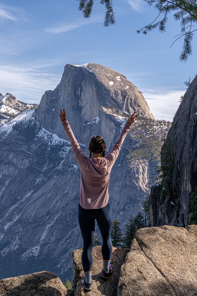 Woman posing for a picture at a viewpoint of Half Dome off Four Mile Trail in Yosemite National Park.