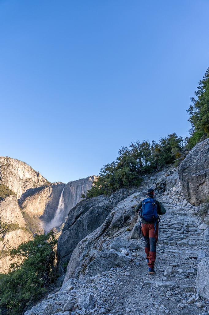 Man hiking along the Four Mile Trail with Yosemite Falls in the background.
