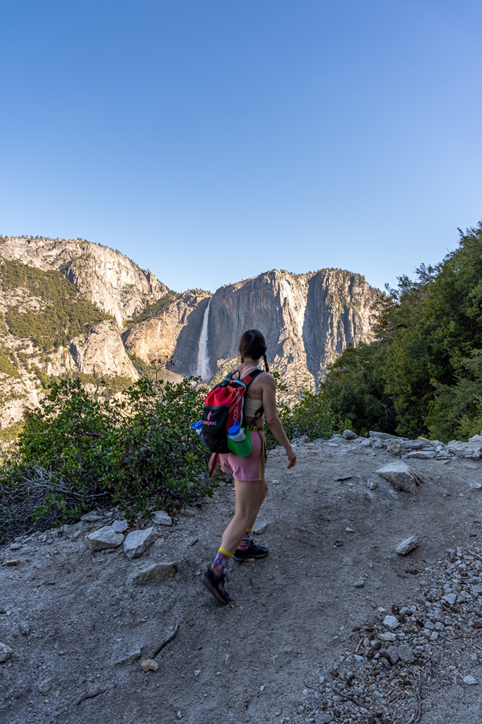 Woman hiking along the Four Mile Trail in Yosemite National Park with Yosemite Falls in the background.