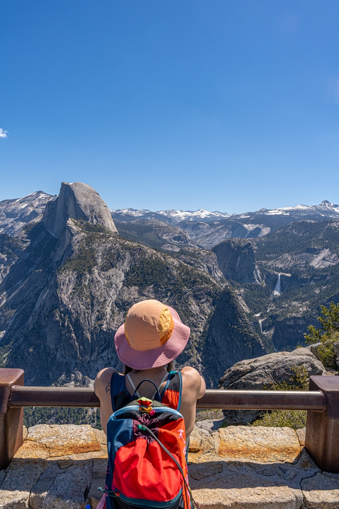 Woman looking at the views of Half Dome, Vernal and Nevada Falls, and other granite peaks in Yosemite National Park from Glacier Point Overlook.