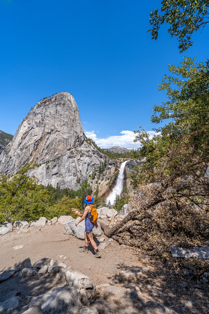 Woman hiking the John Muir Trail with Nevada Fall and Liberty Cap in the background in Yosemite National Park.