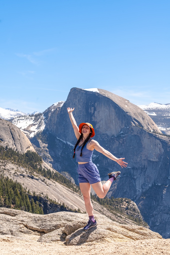 Woman posing for a picture on Yosemite Point with Half Dome in the background.