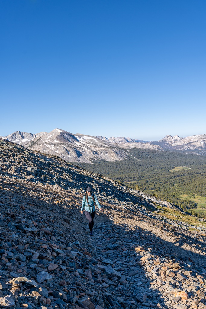 Woman hiking along the Mount Dana Trail near the summit with peaks in the distance.