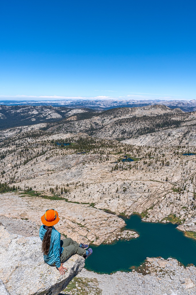 Picture of a woman sitting on a ledge at Mount Hoffmann with an alpine lake in the distance in Yosemite National Park, and it's linked to the California Travel Guide page.