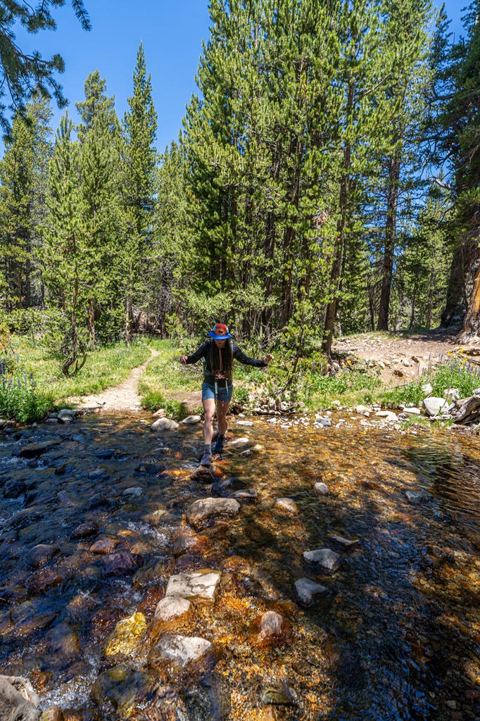 Woman rock hopping to cross the Dana Fork along the Mono Pass Trail in Yosemite National Park.