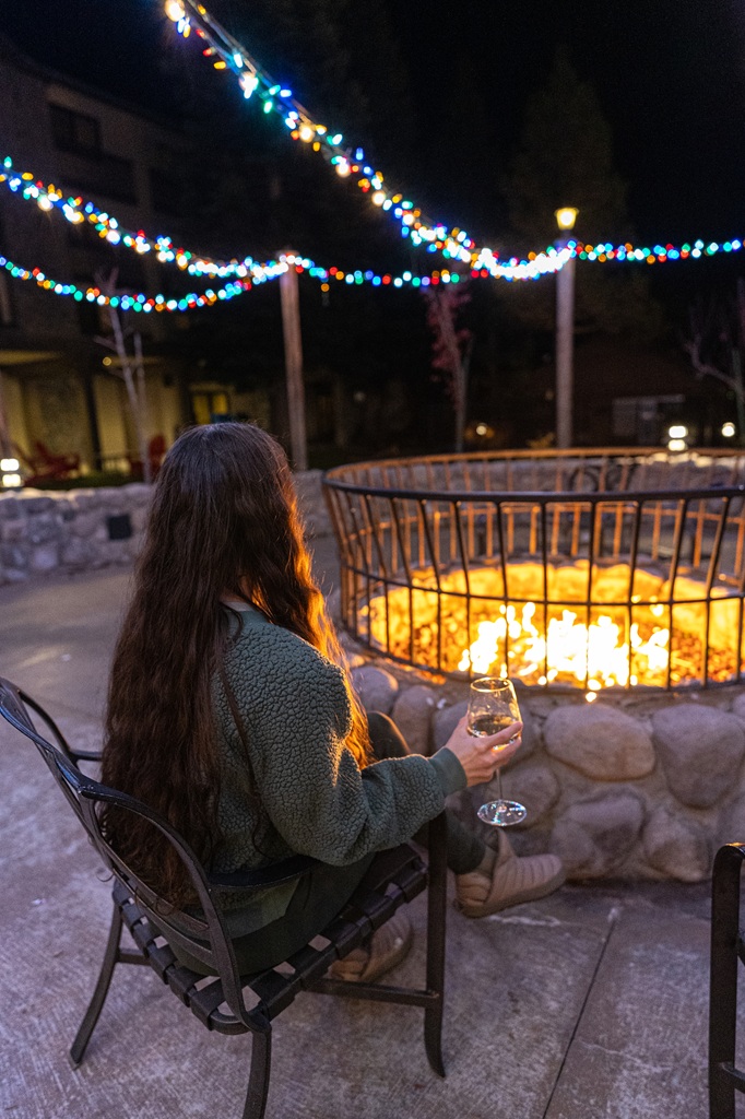 Woman sitting by a fire pit at Tenaya Lodge wearing a green cozy sweater, fleece leggings, and tan thermal booties.