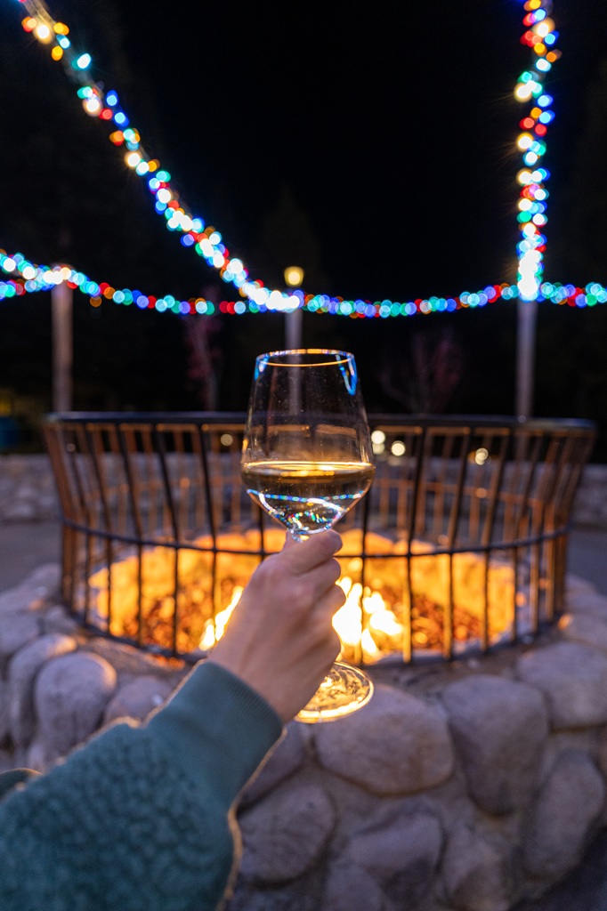 Glass of wine with fire pit and holiday lights in the background at Tenaya Lodge.