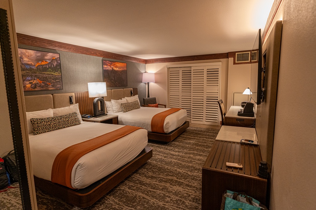 Tenaya Lodge premium room with a patio showing 2 queen beds, desk, wall-mounted tv, and dresser, and beautiful pictures of Yosemite.