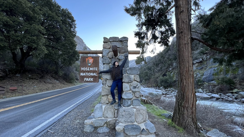 Woman posing in front of the Yosemite National Park sign at Arch Rock Entrance.