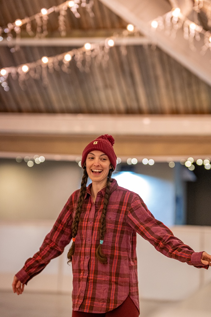 Woman wearing a cozy plaid long sleeve shirt, fleece leggings, and a red beanie while ice skating at Tenaya Lodge.