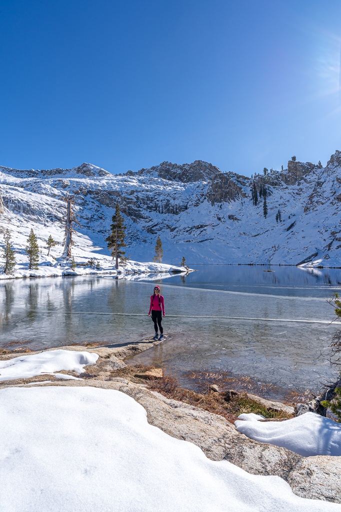 Woman standing on a rock in front of Pear Lake covered in snow and ice in Sequoia National Park.