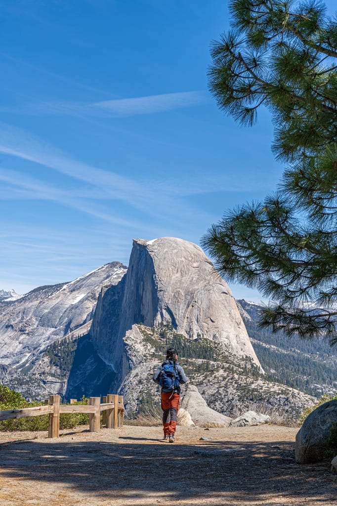 Man walking on a trail at Glacier Point with Half Dome in the distance.