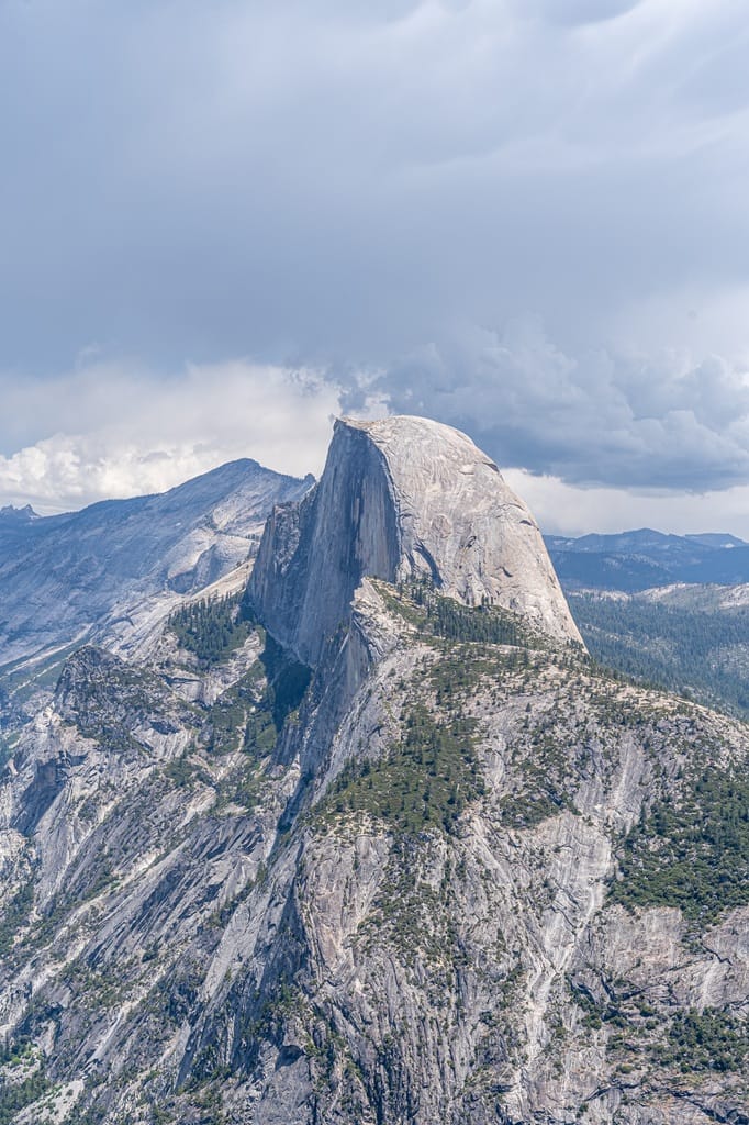 View of Half Dome and Clouds Rest seen from Glacier Point on a cloudy day in Yosemite National Park.