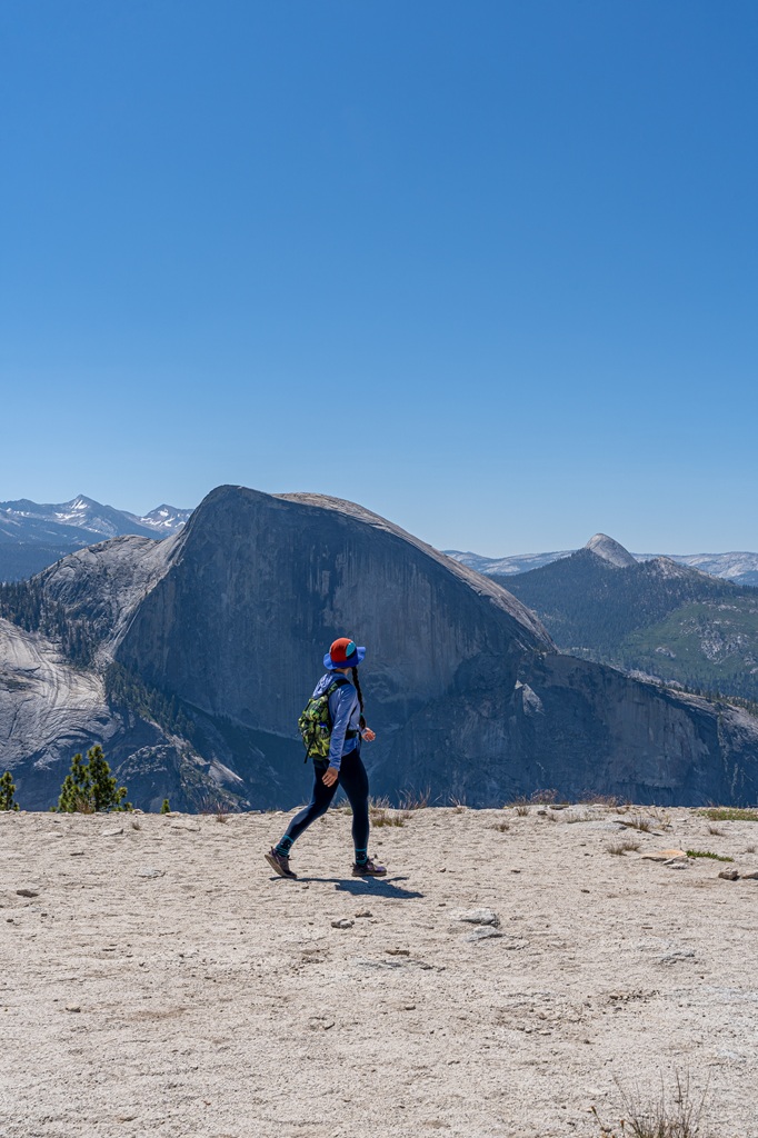 Woman hiking towards North Dome with Half Dome and High Sierra peaks in the distance.