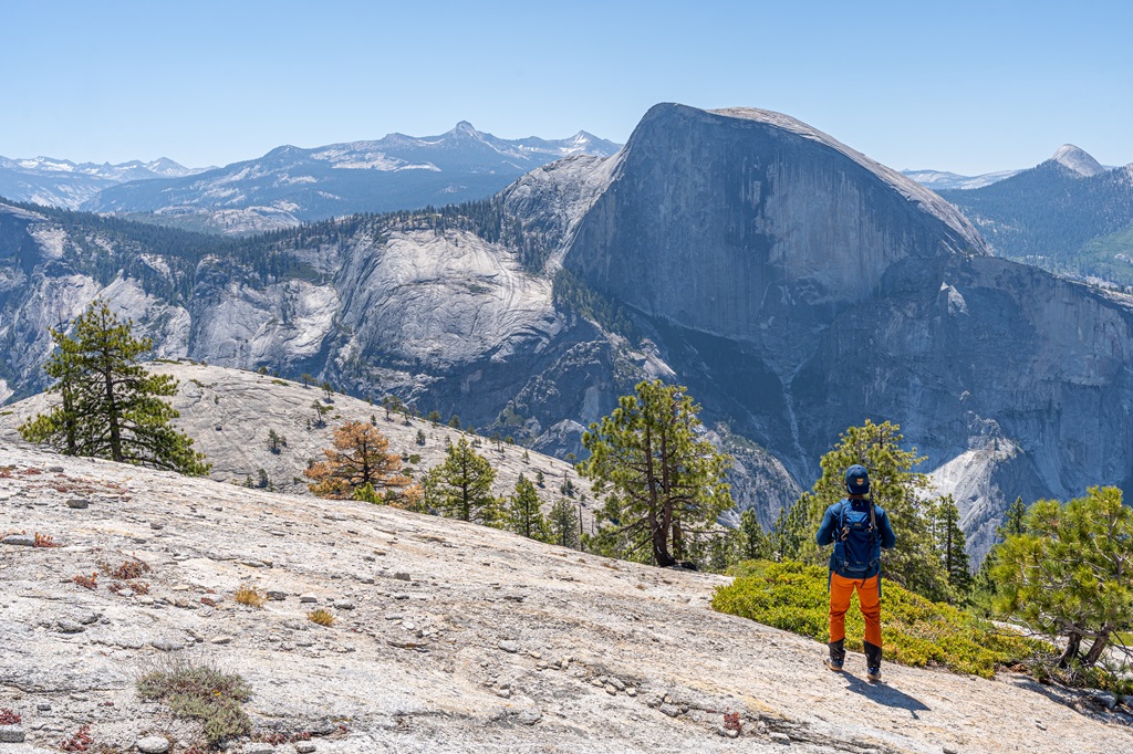 Man looking at views of Half Dome, Basket Dome, and other granite peaks seen from North Dome Trail.