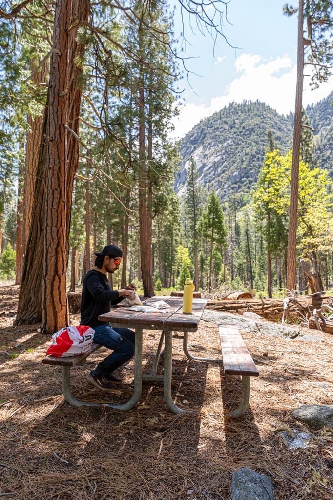 Man sitting at a picnic table eating a snack at Road's End in Kings Canyon National Park.