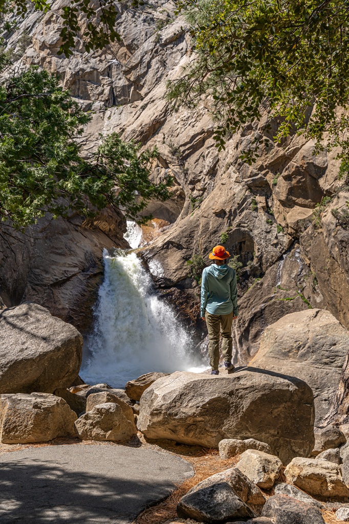 Woman standing on a rock looking at Roaring River Falls in Kings Canyon National Park.