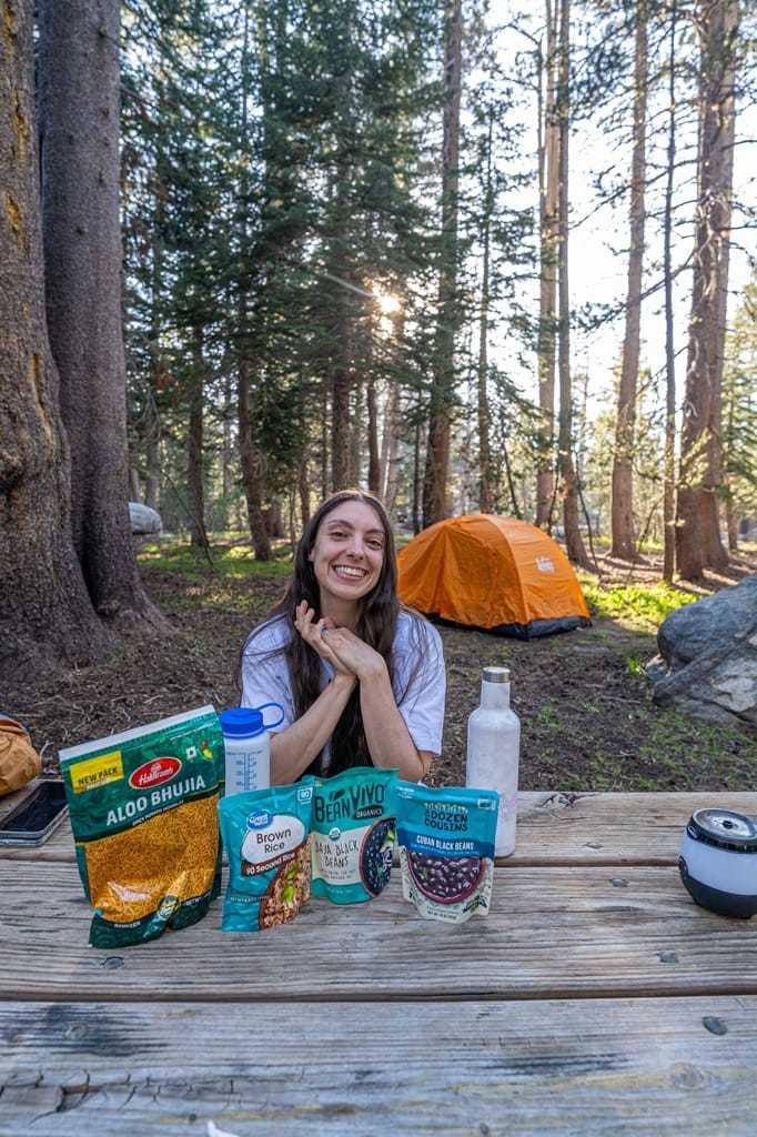 Woman sitting at picnic table with food in front and tent in the background at White Wolf Campground in Yosemite.