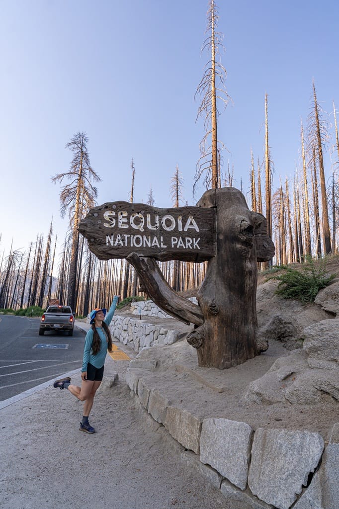 Woman posing for a picture beside the Sequoia National Park sign.
