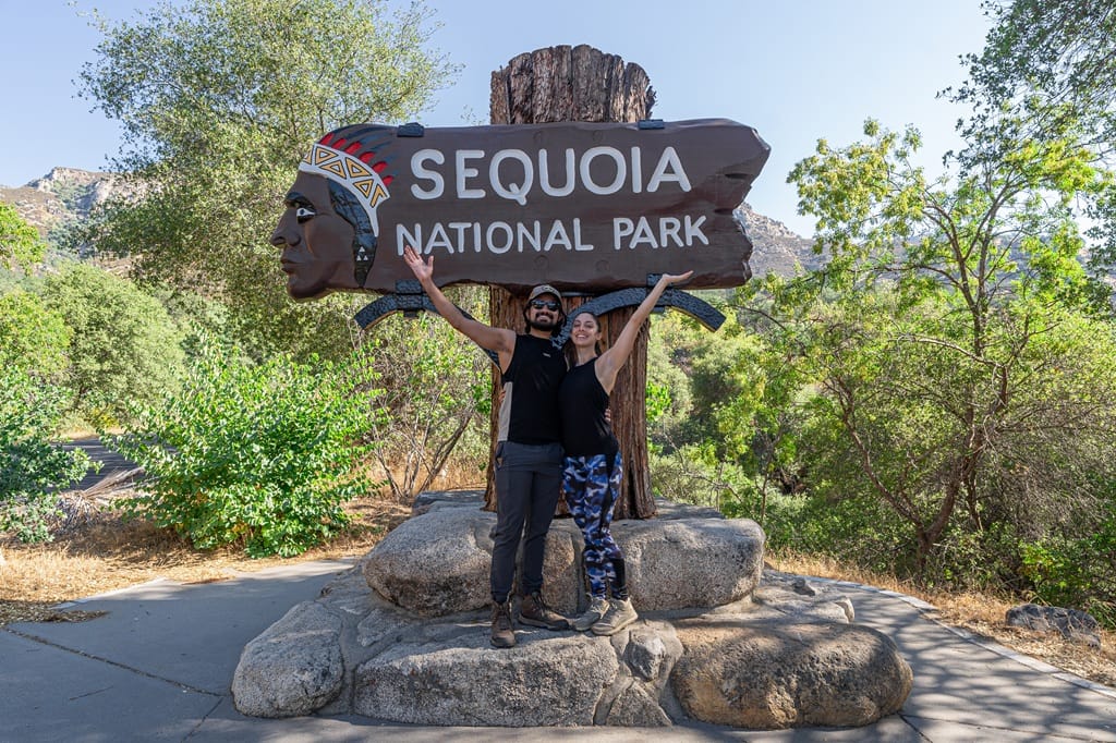 Man and woman posing for a picture in front of the Sequoia National Park sign near the Ash Mountain Entrance.
