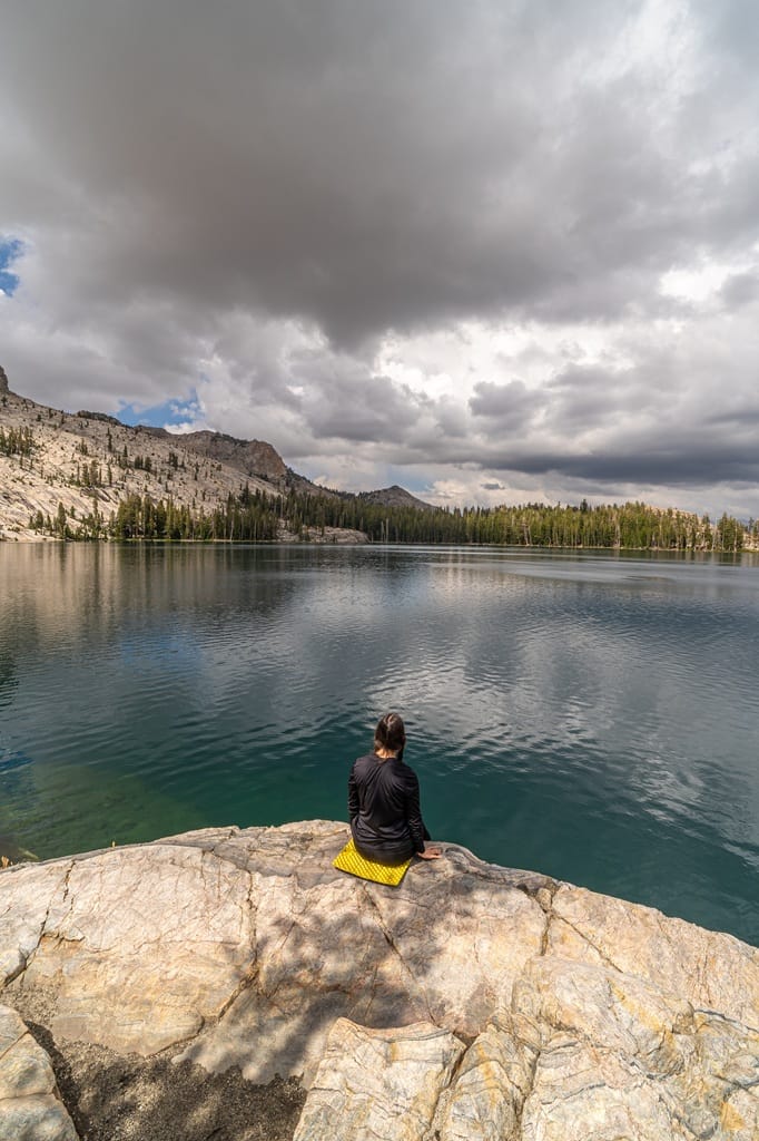 Woman sitting on the granite shore at May Lake with dark clouds above in Yosemite National Park.