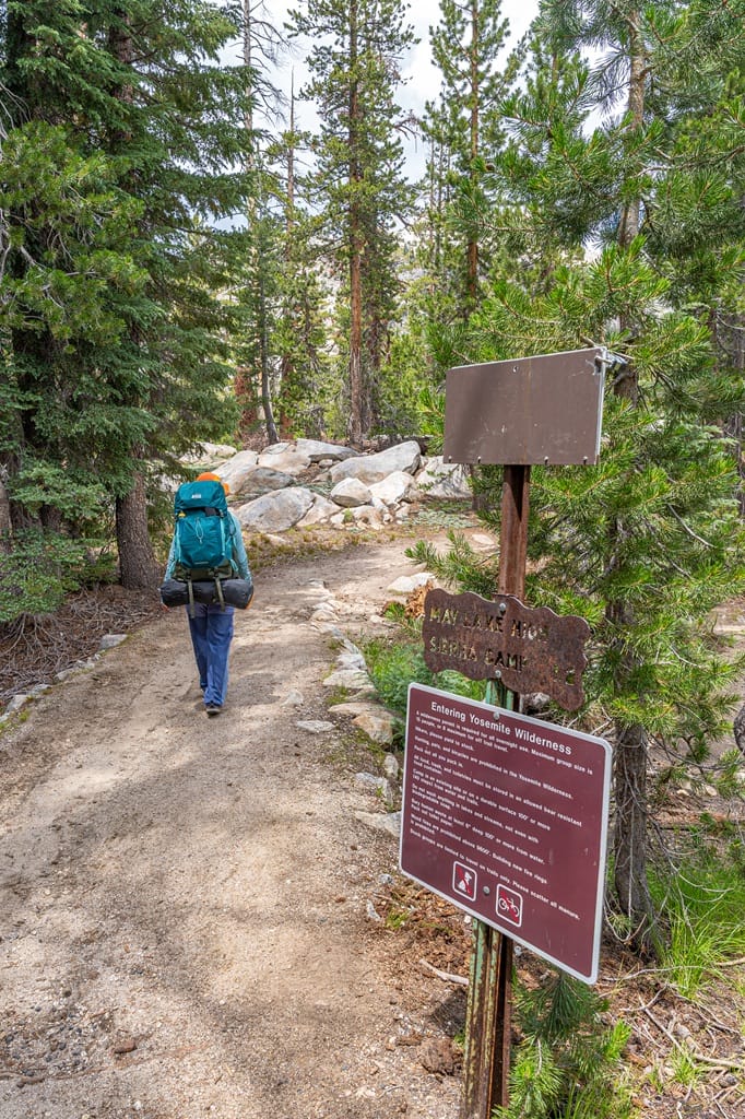 Woman hiking along the May Lake Trail past the trailhead sign in Yosemite National Park.