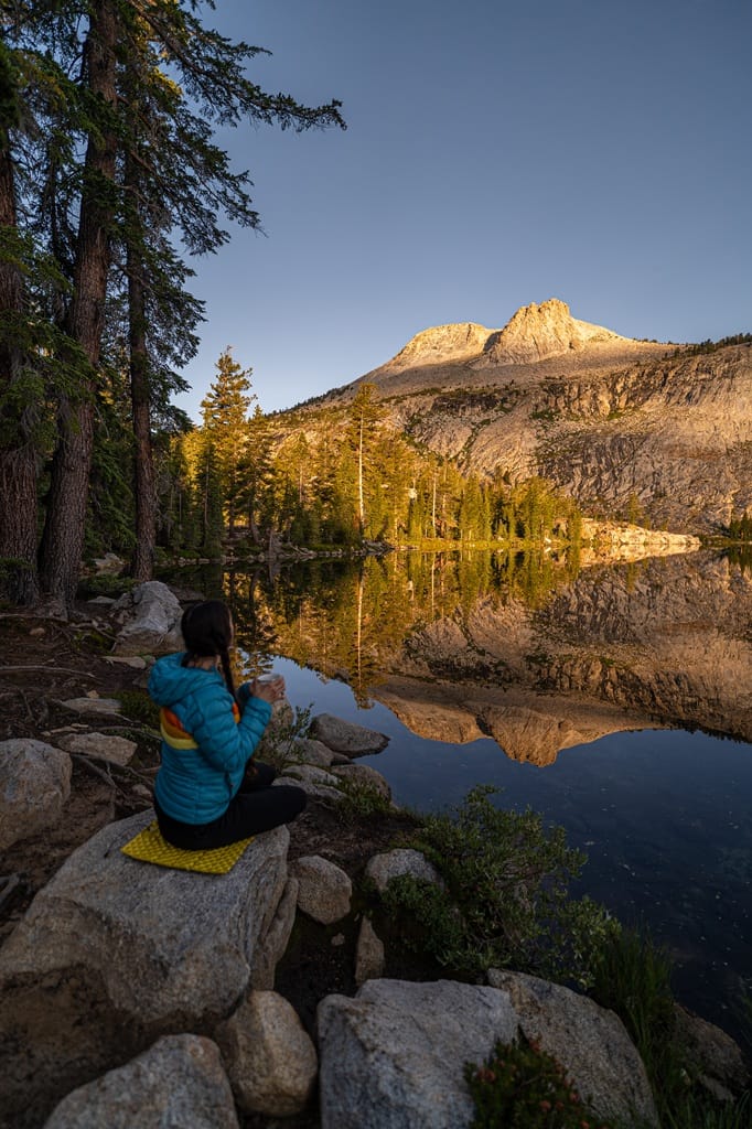 Woman sitting on a rock drinking tea and watching the sunrise from May Lake in Yosemite National Park.